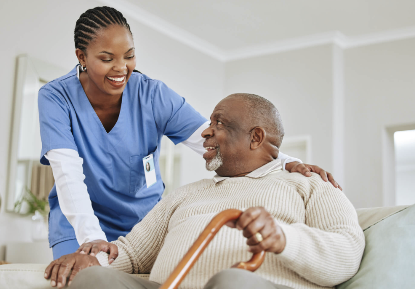 A Black caregiver smiling with an older client during a supportive visit at home